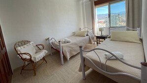 Un dormitori amb dos llits, una cadira i una finestra amb vista a la ciutat.