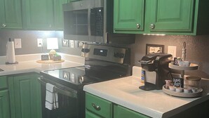 A kitchen with green cabinets, a black microwave, and a coffee maker.