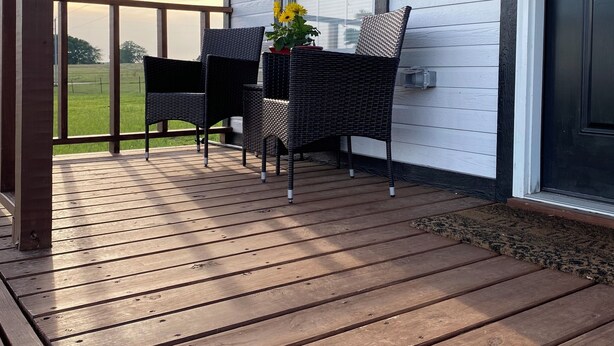 A wooden deck with two wicker chairs and a small table, a potted plant with yellow flowers, and a door with a keypad lock.