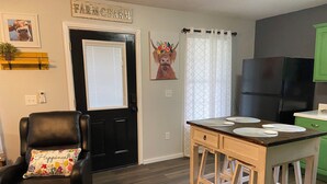 A modern kitchen with a wooden island, a black leather chair with a floral pillow, a black refrigerator, and a green cabinet.
