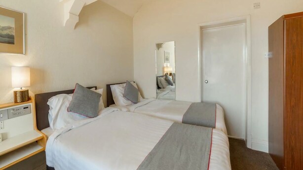 A hotel room with a bed, bedside table, lamp, and a wardrobe. - Cumberland Hotel (Workington)