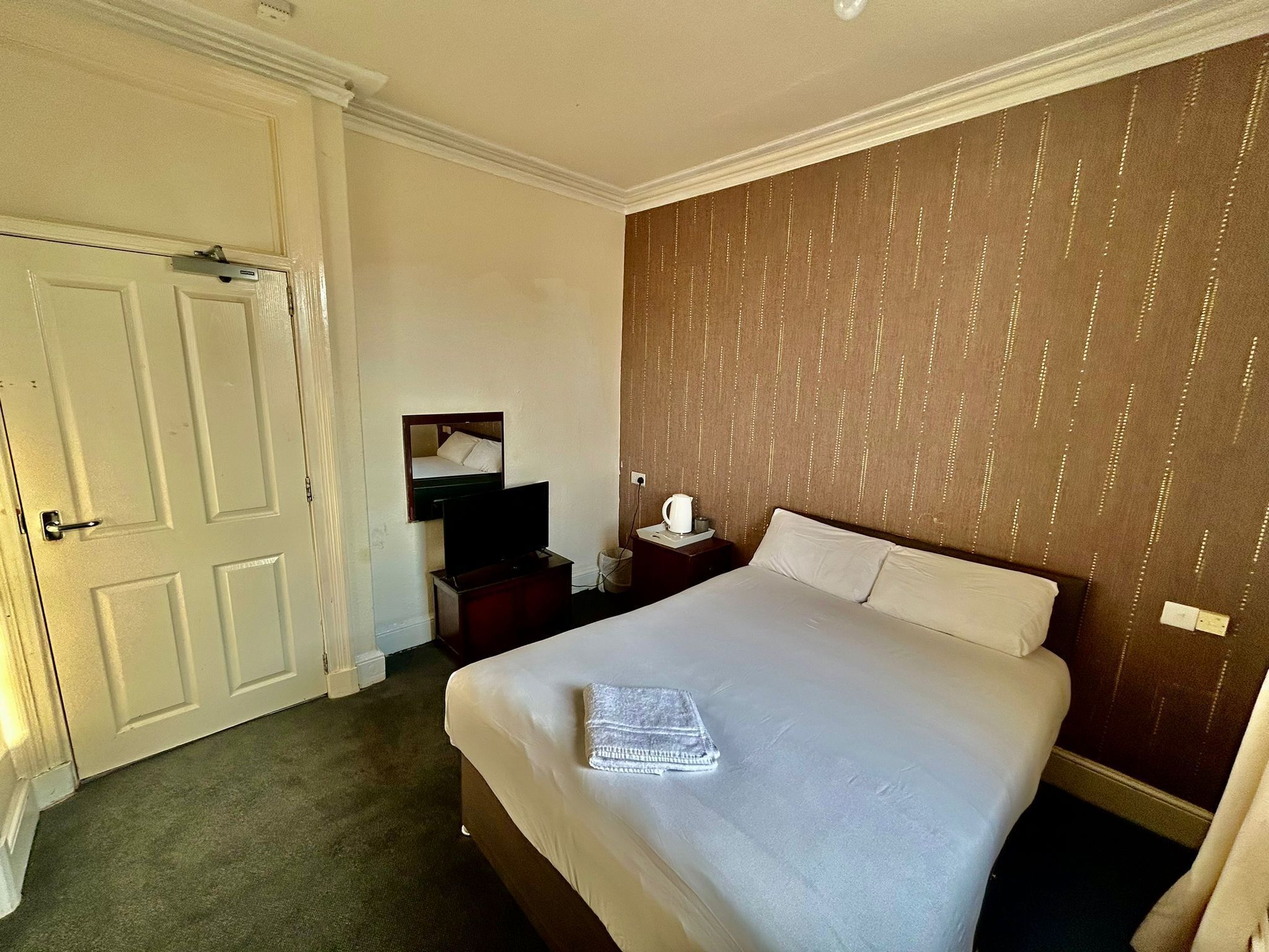 A hotel room with a large bed, a dresser, a television, and a mirror.