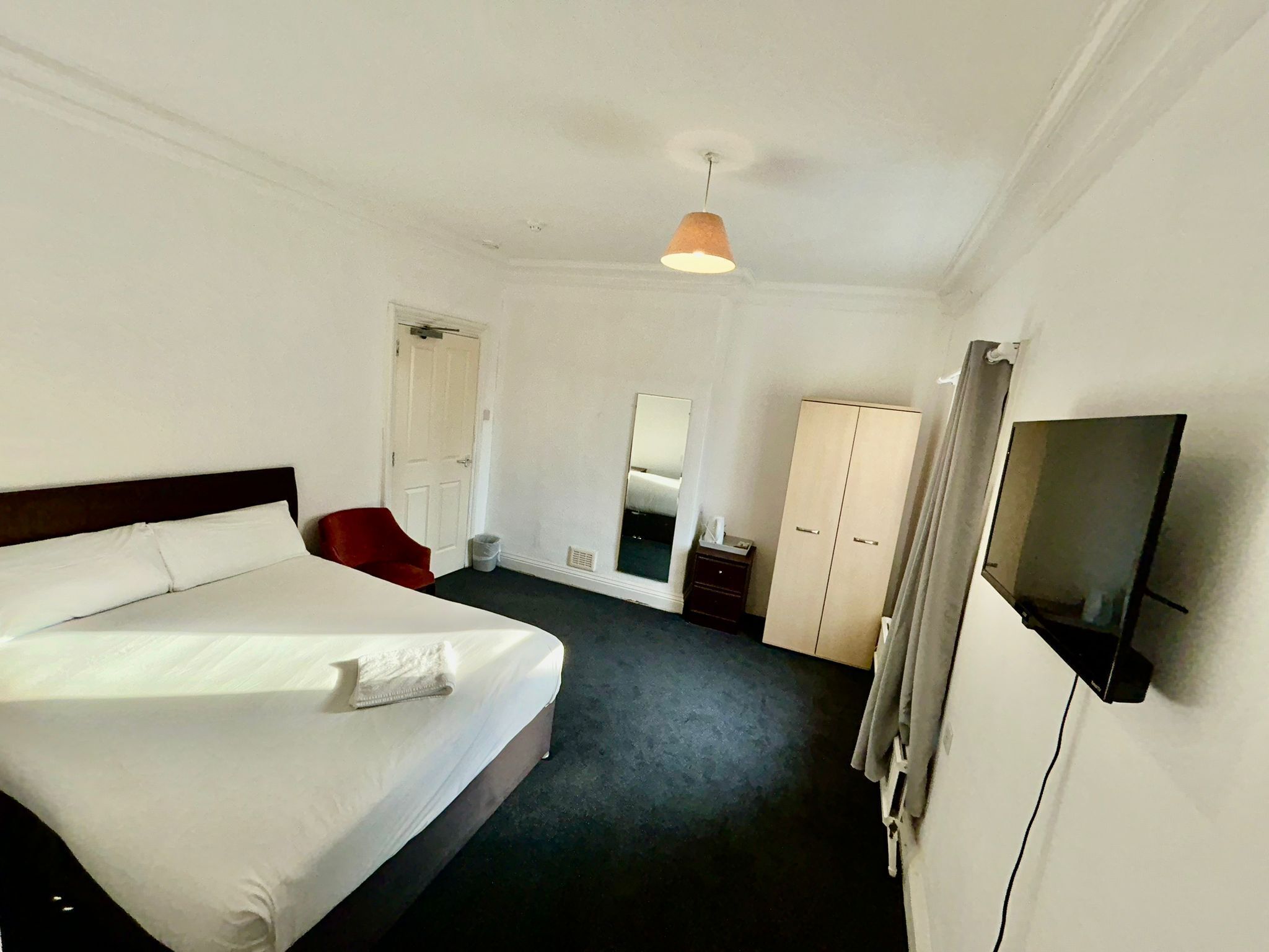 A hotel room with a large bed, a wardrobe, a television, and a mirror.
