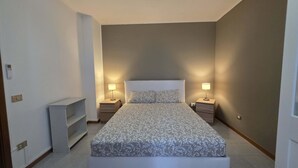Een slaapkamer met een bed, twee nachtkastjes, een wandthermostaat en een plank.