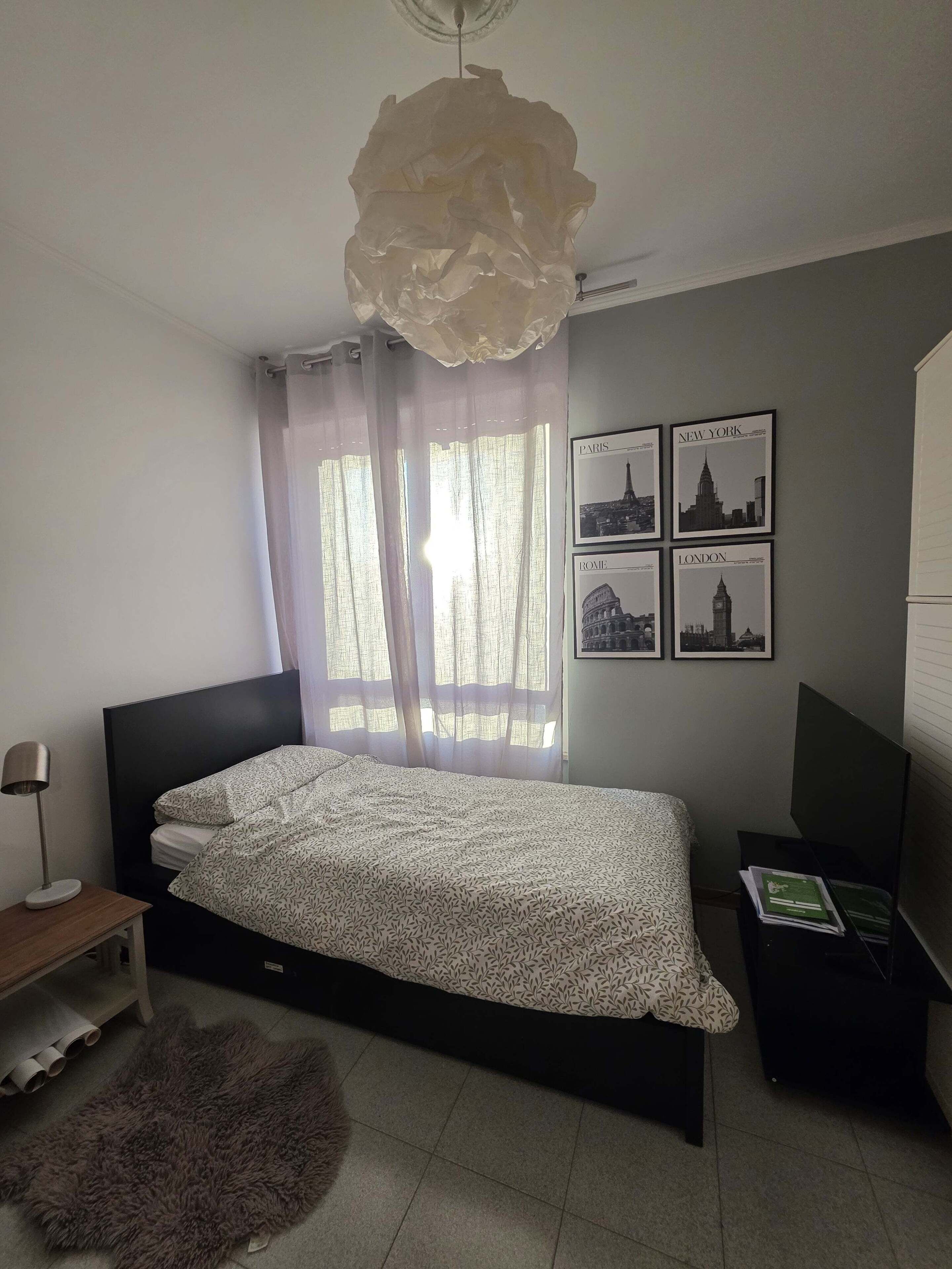 Un dormitorio con cama, escritorio, silla, alfombra y una pared con imágenes de la ciudad.