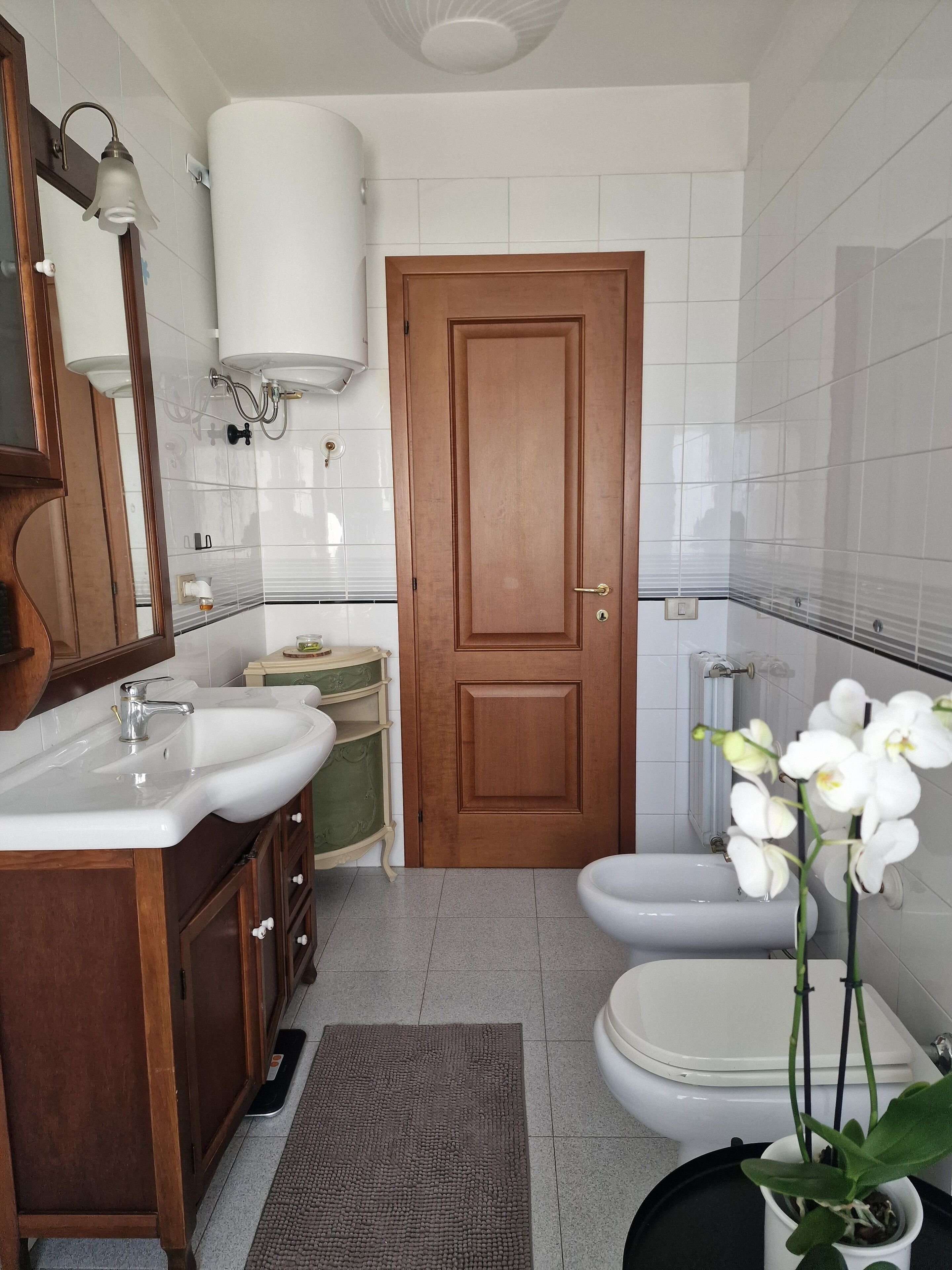 Un baño con puerta de madera, un lavabo blanco, un inodoro y un espejo.