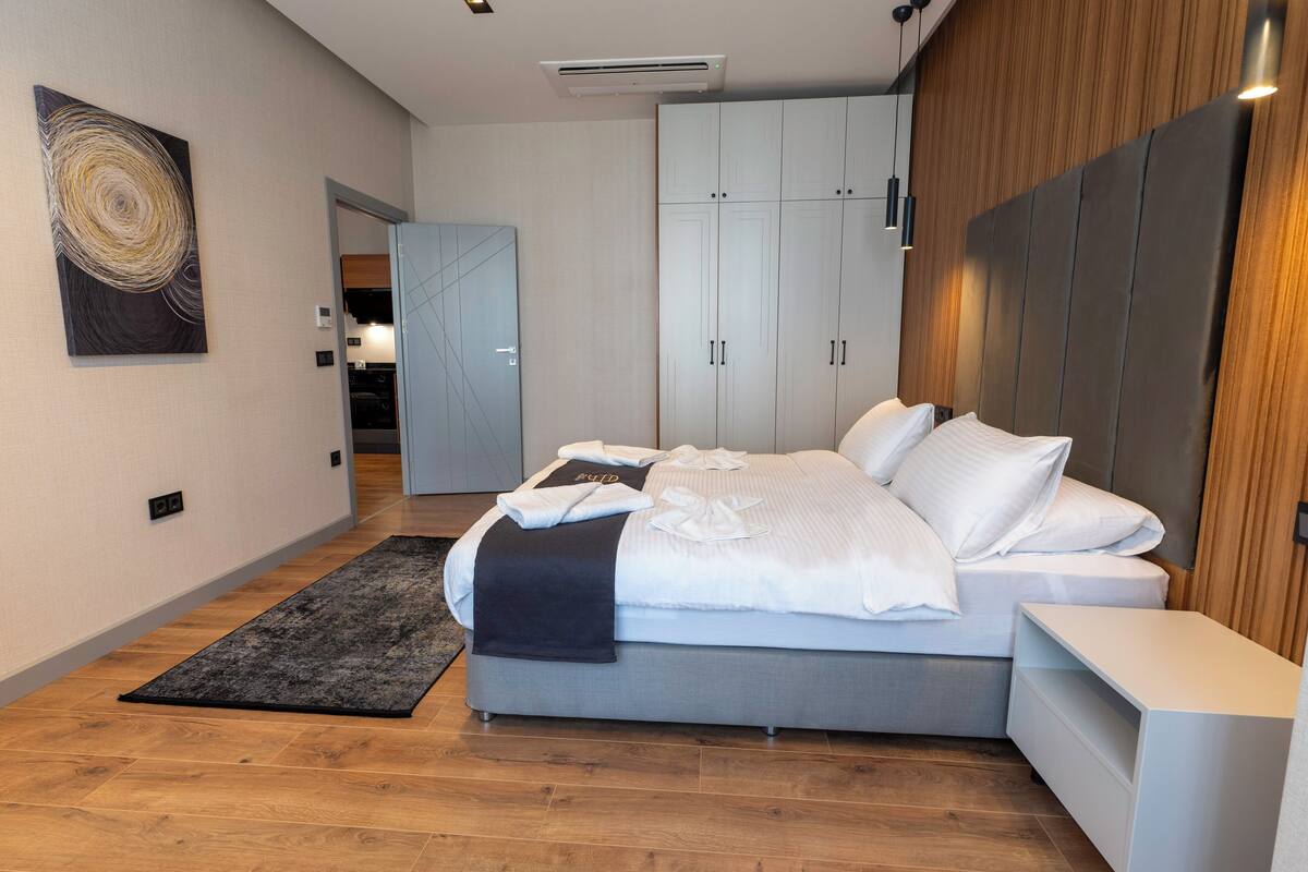 A modern bedroom with a large bed, a wardrobe, and a small bedside table.