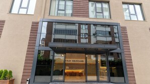 A modern building with a glass entrance, a sign reading "TRAY REZIDANS," and a small outdoor seating area with plants. - TRAY TRABZON  (Yomra)
