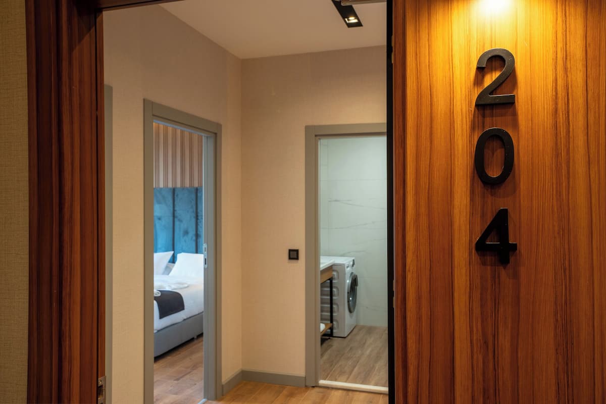 A hotel room with a bed, a washing machine, and a wooden door with the number 204.