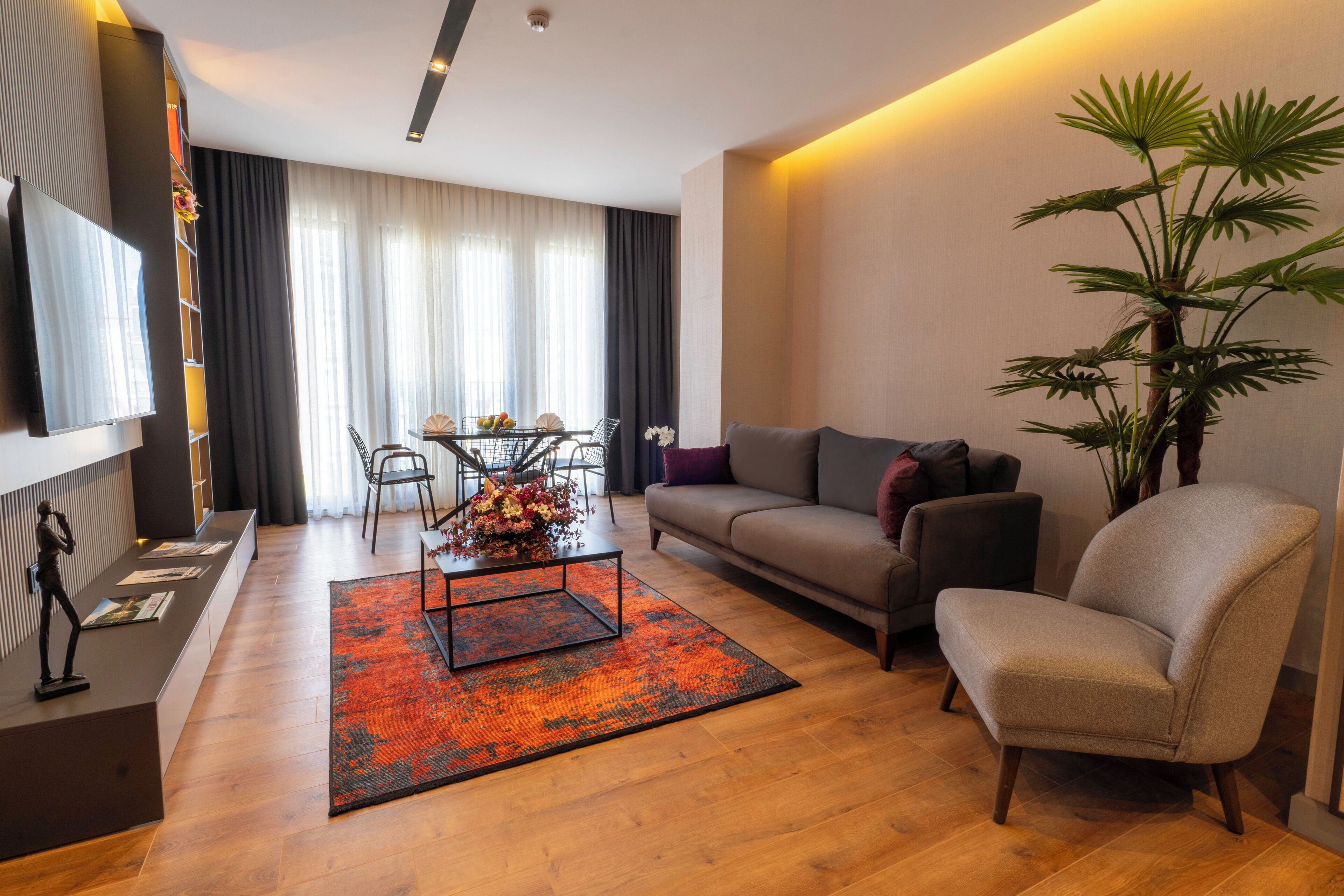 Uma sala de estar moderna com um sofá, poltrona, mesa de centro e uma grande planta em vaso.