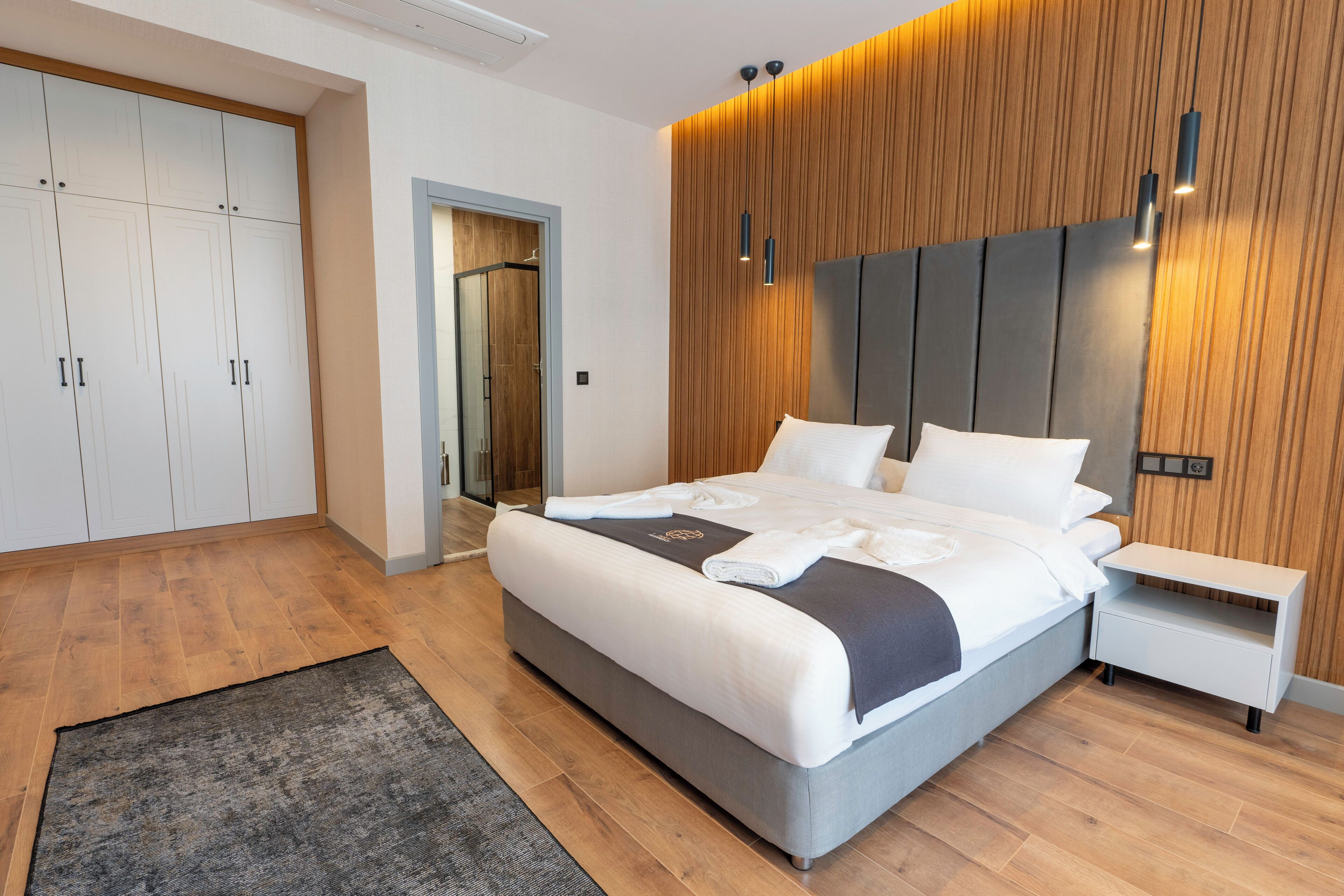 A modern bedroom with a large bed, wooden panel wall, and built-in wardrobe.