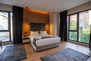Un dormitorio moderno con una cama grande, cabecera de madera y vistas a edificios a través de amplios ventanales.