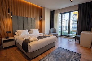 Habitación de hotel moderna con una cama grande, un escritorio, una silla y vistas de la ciudad a través de amplios ventanales.