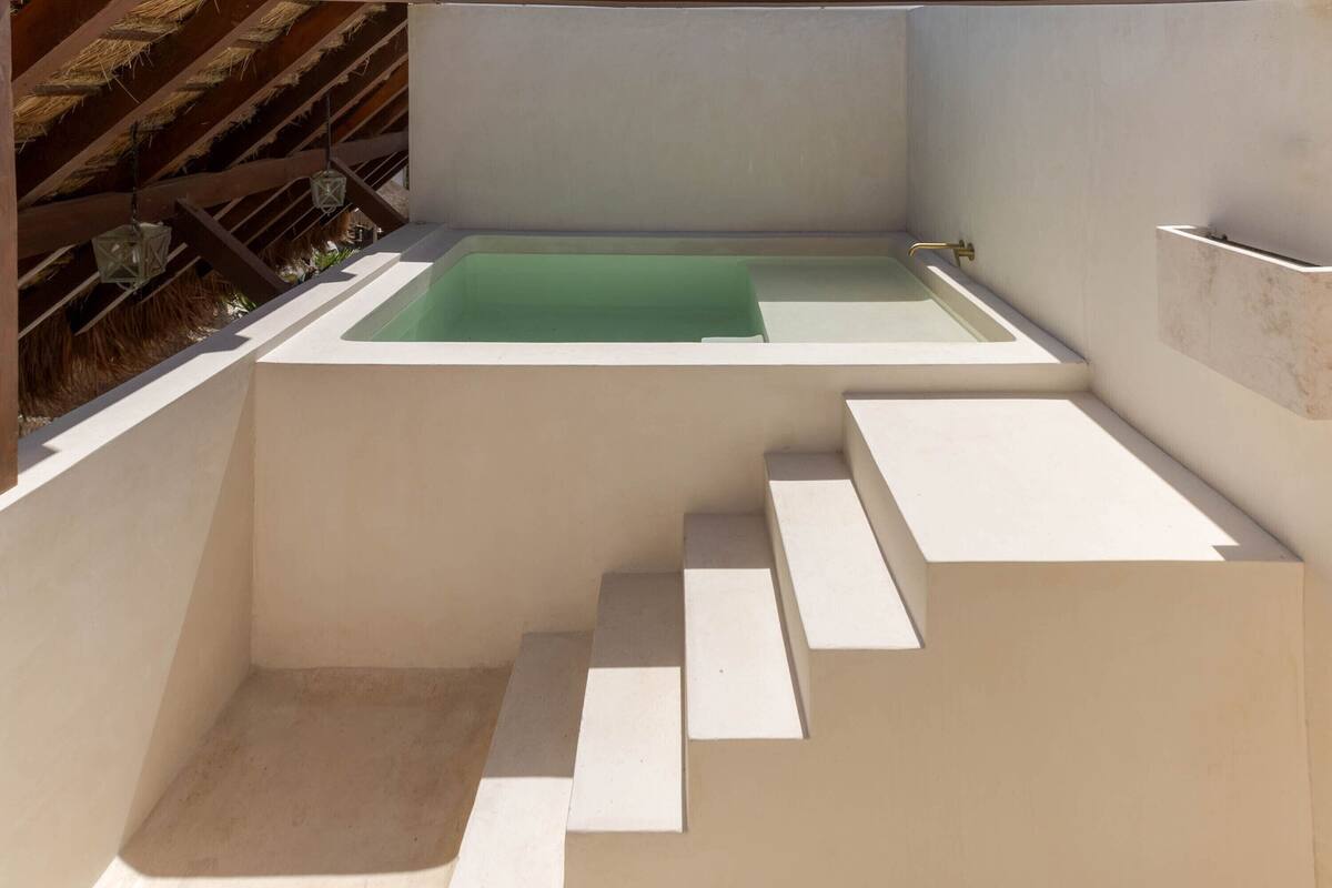 Un baño moderno y minimalista con una bañera independiente, una zona de ducha pequeña y un conjunto de escalones que conducen a una plataforma elevada.