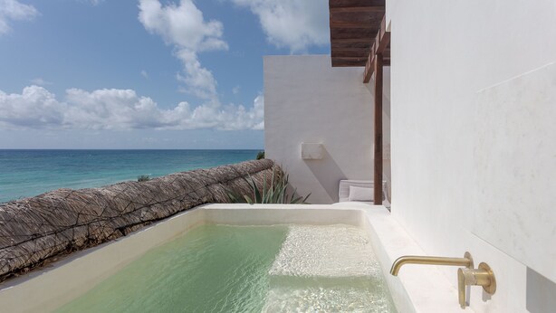Une piscine privée à l’eau turquoise et limpide, un mur en pierre et un plafond en bois.