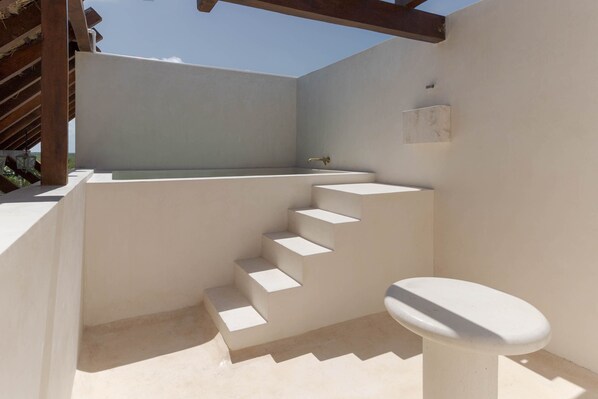 A modern outdoor bathroom with a built-in bathtub, a toilet, and a set of stairs leading to a higher level. - Suites Panamera (Tulum)