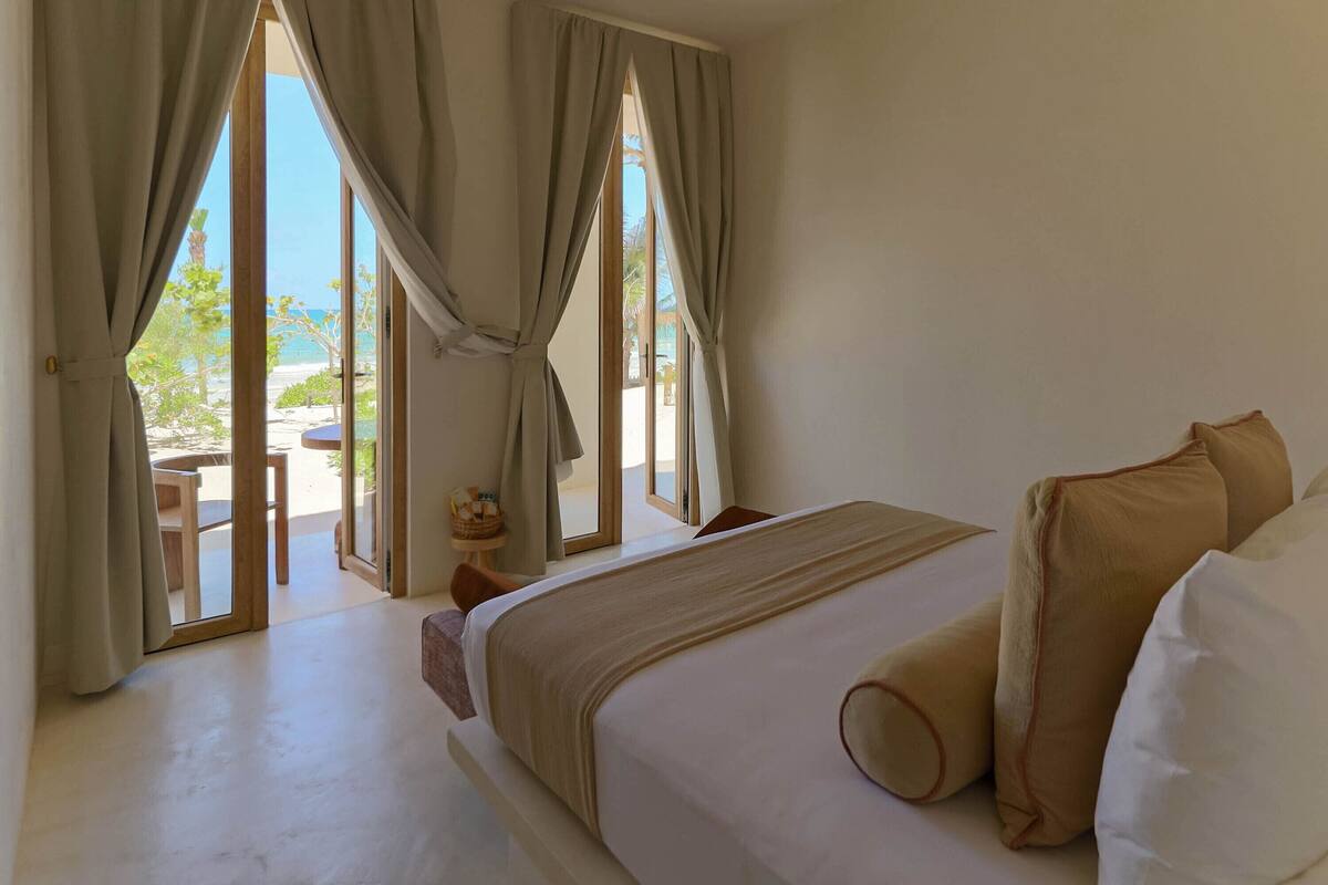 Una habitación de hotel con una cama grande, cortinas color beige y vista a la playa.