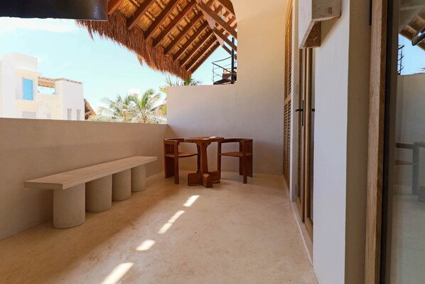 Un balcon avec une table et des chaises en bois, un banc et un toit de chaume.