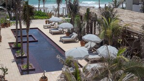 Un espace piscine agrémenté de chaises longues et de parasols, entouré de palmiers et offrant une vue sur l’océan.