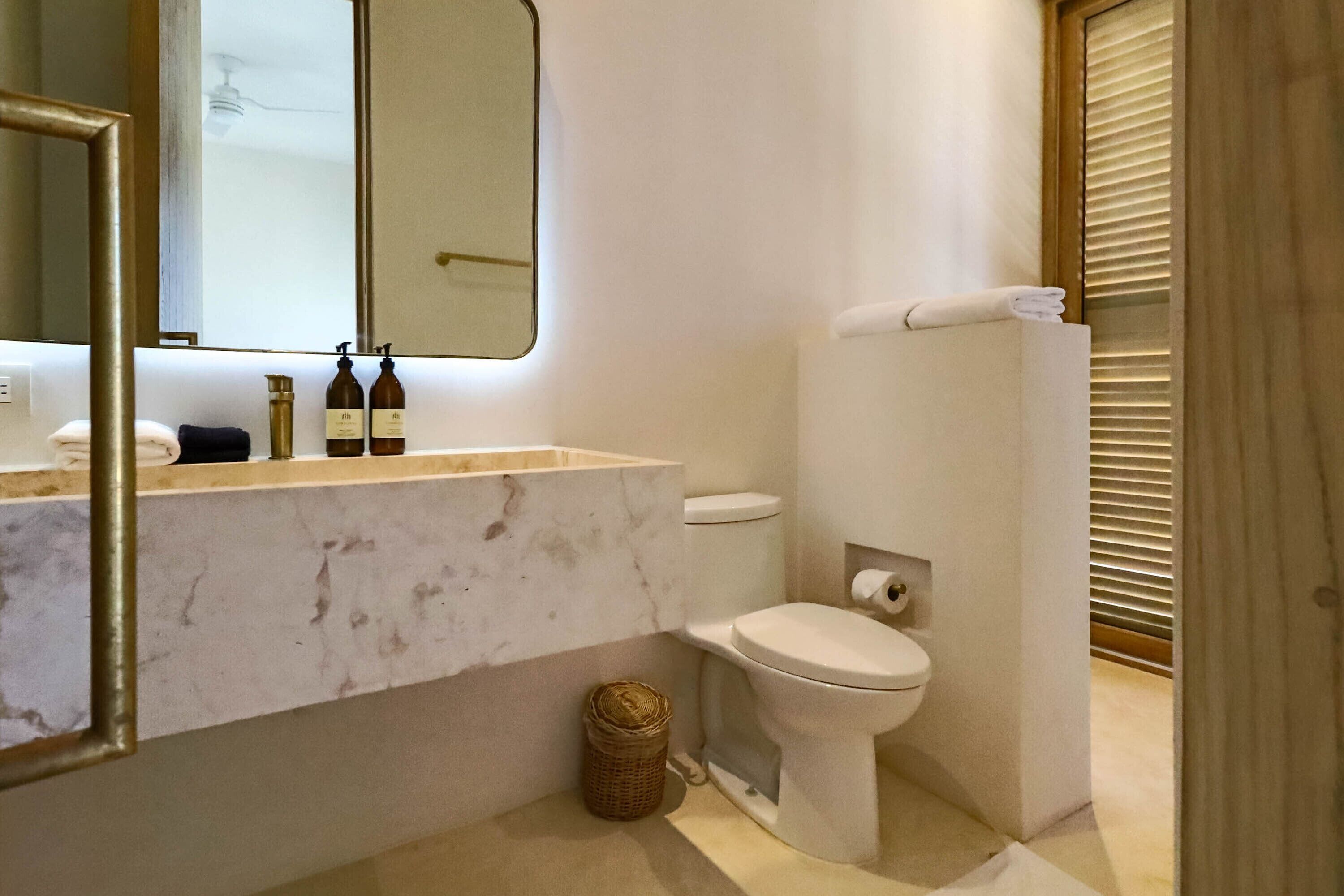 A modern bathroom with a marble sink, a toilet, and a mirror.