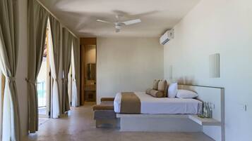 A bedroom with a bed, a ceiling fan, an air conditioning unit, and a bathroom visible through an open door.