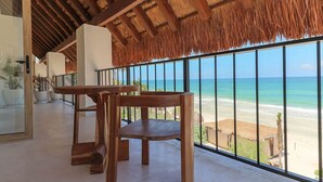 Une table et des chaises en bois sont disposées sur un balcon d’où l’on a vue sur la plage.