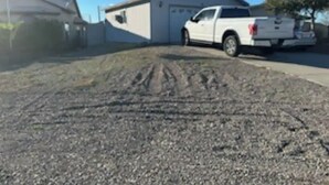 En grusvej fører hen til en garage, hvor der holder en hvid pickup truck i nærheden.