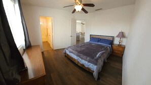Ein Schlafzimmer mit Bett, Holzboden, Deckenventilator und Nachttisch mit Lampe.