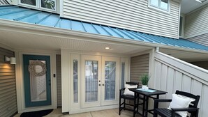 A covered patio area with a door, two chairs, a small table, and a potted plant. - ServingSand West @ SeaColony: Carriage House between Tennis and Fitness Center! (Bethany Beach)