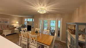 A dining area with a wooden table and white chairs, a chandelier, and a view through glass doors to the outside. - ServingSand West @ SeaColony: Carriage House between Tennis and Fitness Center! (Bethany Beach)