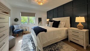 A bedroom with a large bed, bedside tables, a dresser, a window with blinds, a ceiling light, and a view of greenery outside. - ServingSand West @ SeaColony: Carriage House between Tennis and Fitness Center! (Bethany Beach)