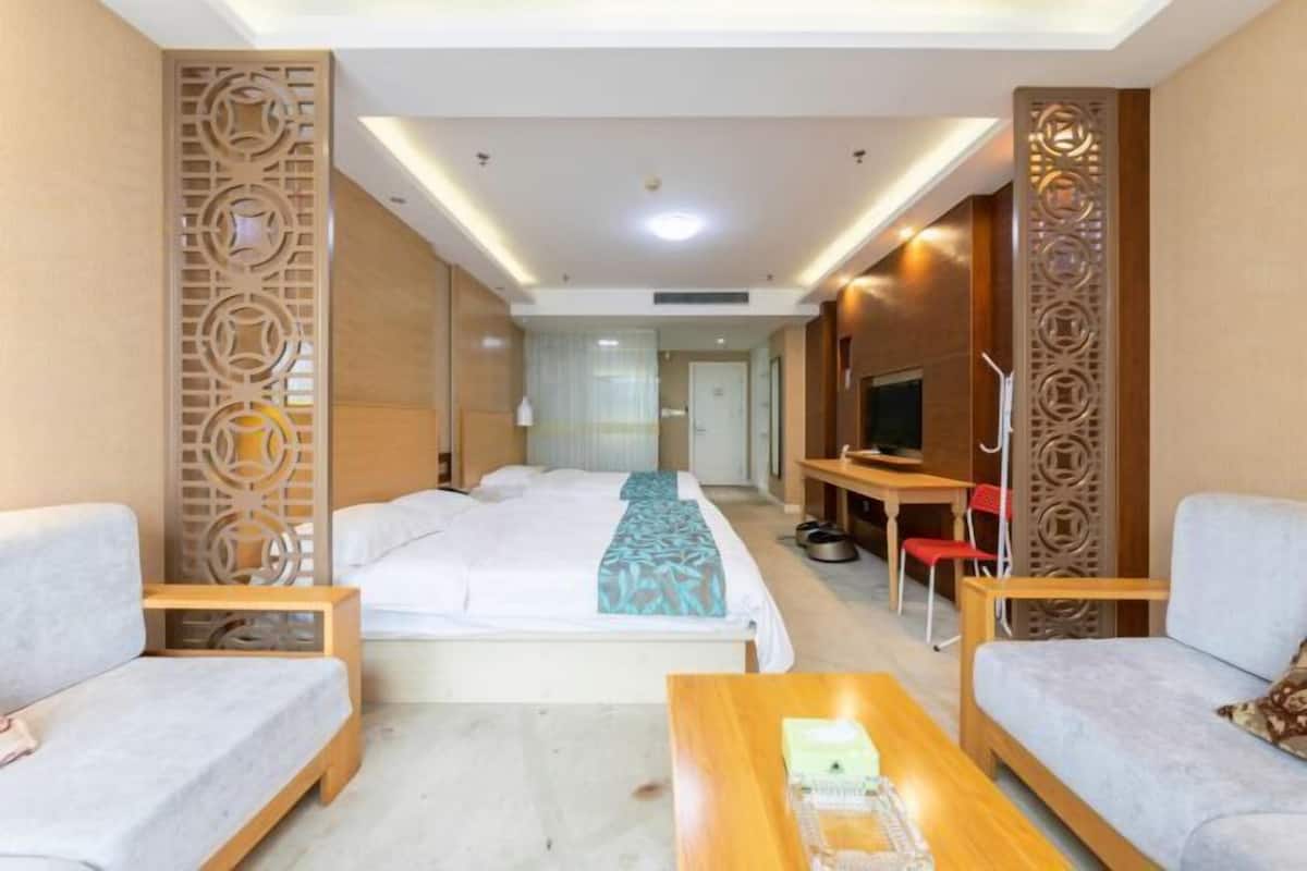 Een hotelkamer met een bed, twee slaapbanken, een salontafel, een televisie en een decoratief wandpaneel.