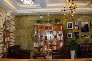 A cozy lounge area with leather sofas, a wooden coffee table, and a large bookshelf filled with books and plants. - Bailisi Hotel (Lianyungang)
