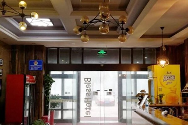 A hotel entrance with a reception desk, a glass door, and a ceiling with hanging lights.