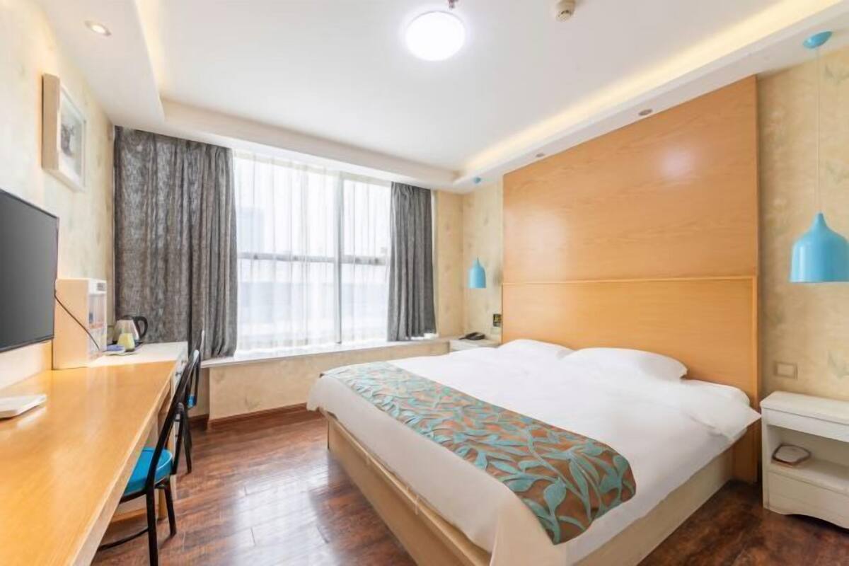 Een hotelkamer met een bed, een bureau, een stoel, een televisie, een raam met gordijnen en een nachtkastje.
