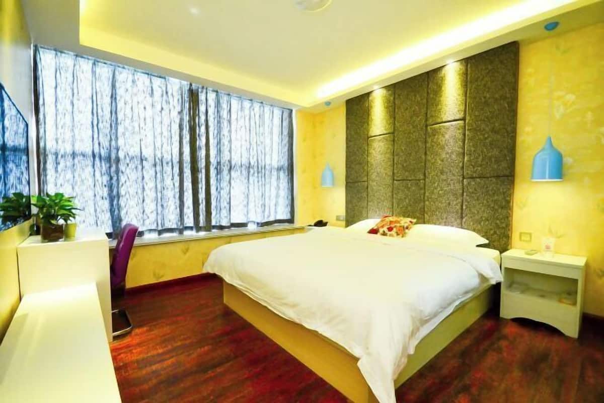 Hotelkamer met een groot bed, nachtkastje, raam met gordijnen en een kamerplant.
