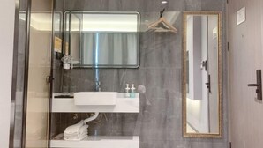 Un baño moderno con cabina de ducha de vidrio, un tocador blanco con espejo y un espejo grande en la pared.