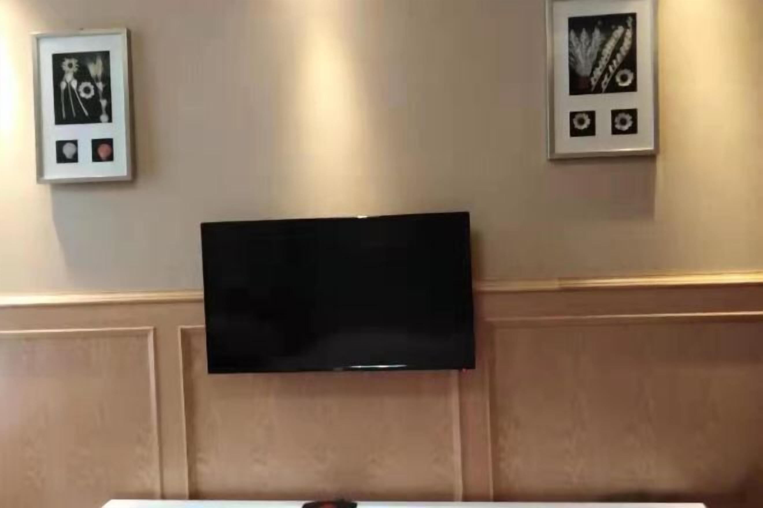 Habitación de hotel con televisor de pantalla plana montado en la pared, diseño de panel de madera y dos cuadros enmarcados.