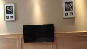 A hotel room with a flat-screen TV mounted on the wall, a wooden panel design, and two framed pictures on the wall. - Bailisi Hotel (Lianyungang)