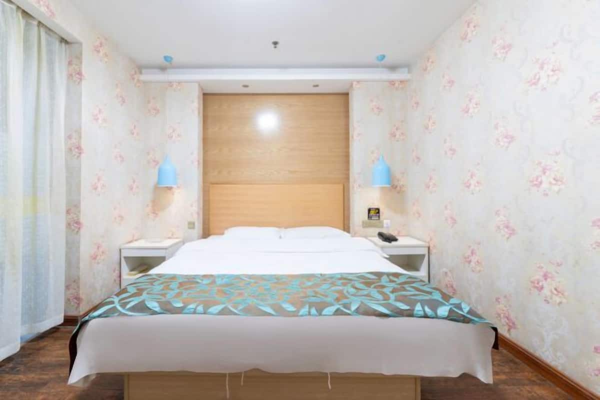 Een hotelkamer met een bed, twee nachtkastjes, een hoofdeinde van hout en bloemenbehang.