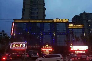 A hotel with multiple illuminated signs, a prominent entrance, and a parking area with cars.