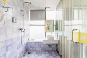 Une salle de bain avec des murs recouverts de carreaux blancs, un sol carrelé de bleu, un lavabo blanc, un miroir et une douche.