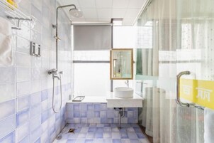 Un baño con paredes de azulejos blancos, suelo de baldosas azules, un lavamanos blanco, un espejo y una ducha.