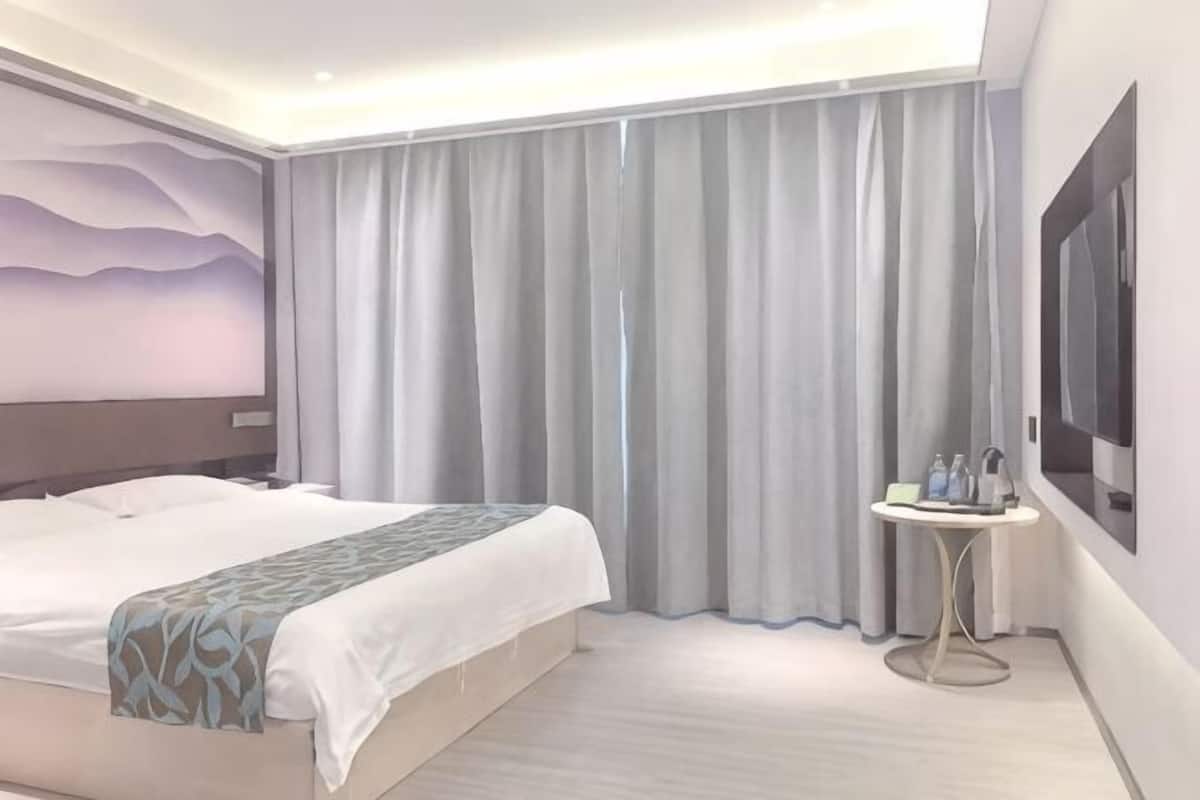 Een hotelkamer met een groot bed, een klein tafeltje met flessen en een schilderij aan de muur.
