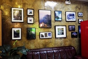 Un mur orné de plusieurs photographies encadrées, un canapé en cuir marron et un objet rouge sur la droite.