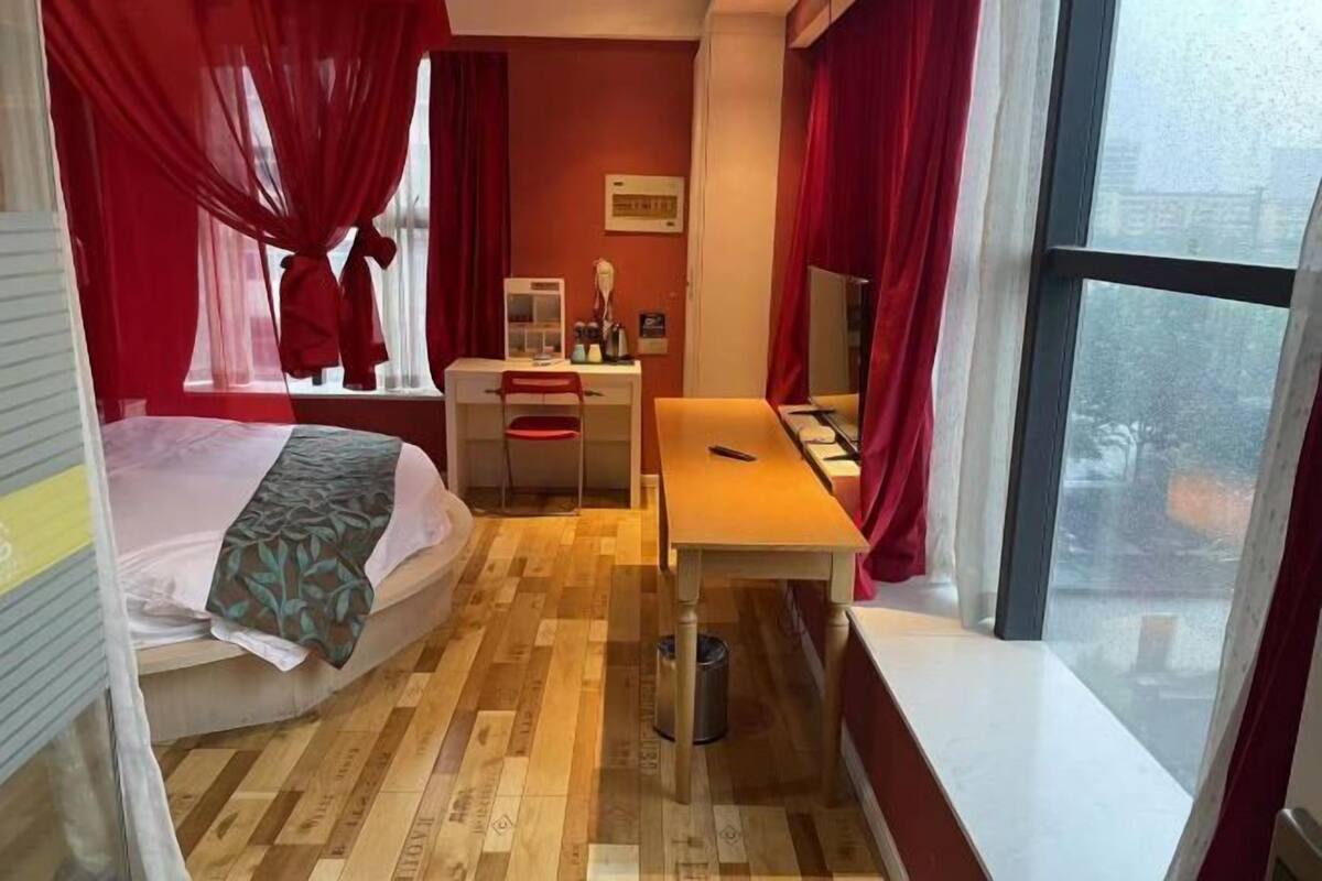 Een kleine hotelkamer met een bed, een bureau, een stoel, een tafeltje en een raam.