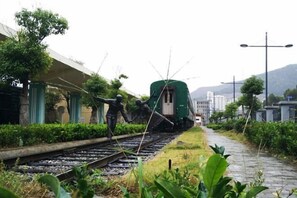 Un train circule sur des voies, avec un wagon vert, entouré de verdure et de bâtiments.