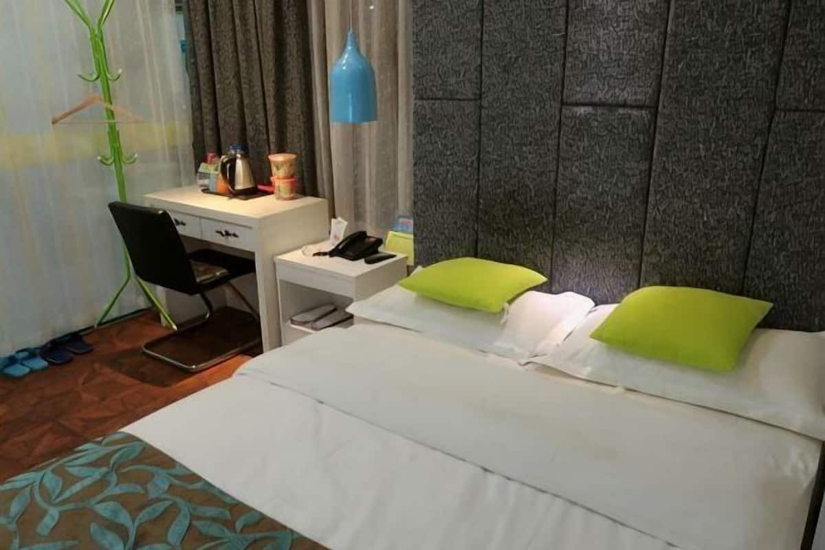 Een hotelkamer met een bed, een bureau, een stoel, een nachtkastje, een lamp en een raam met gordijnen.