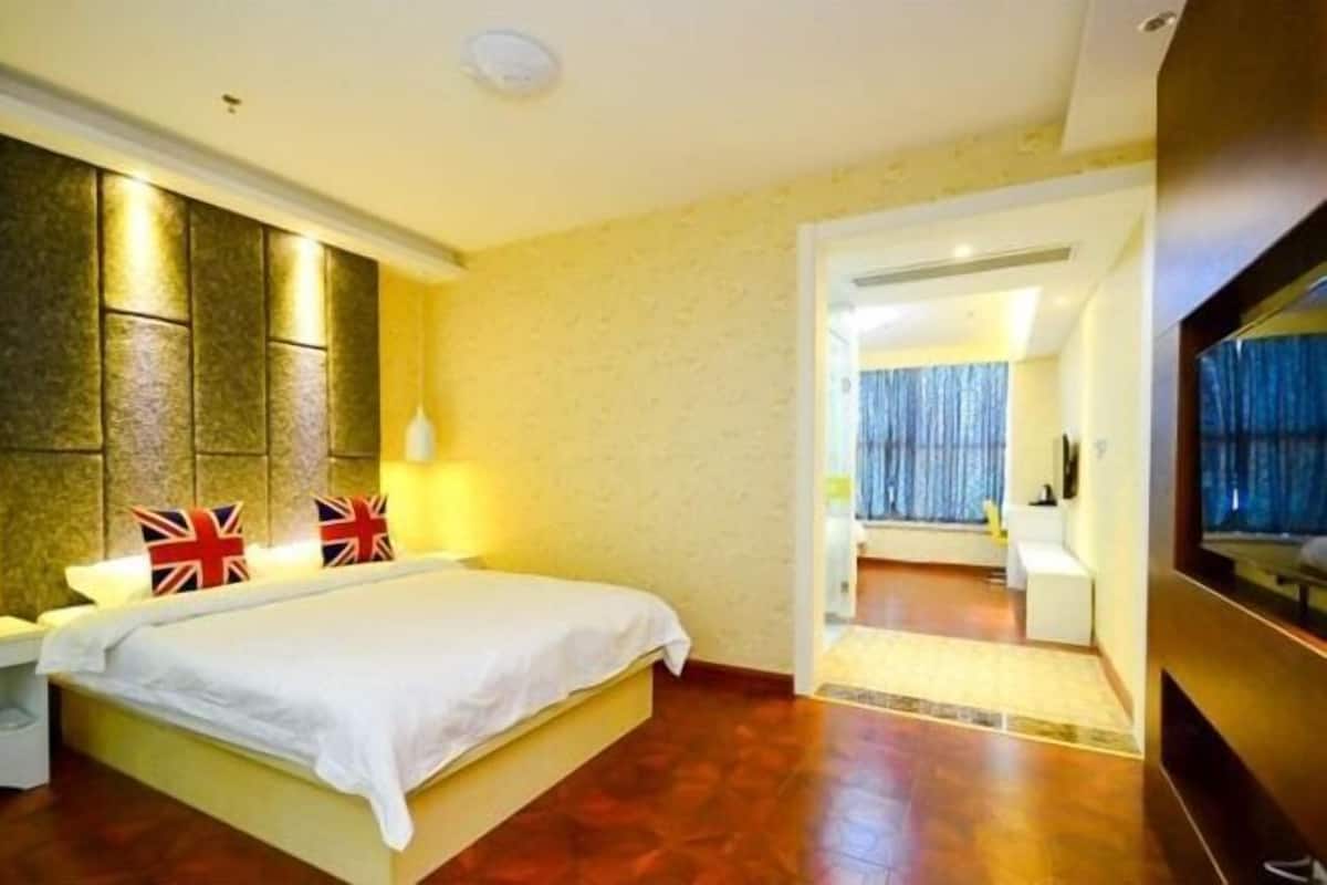 Een hotelkamer met een bed, nachtkastje, een wandlamp en uitzicht op een andere kamer.