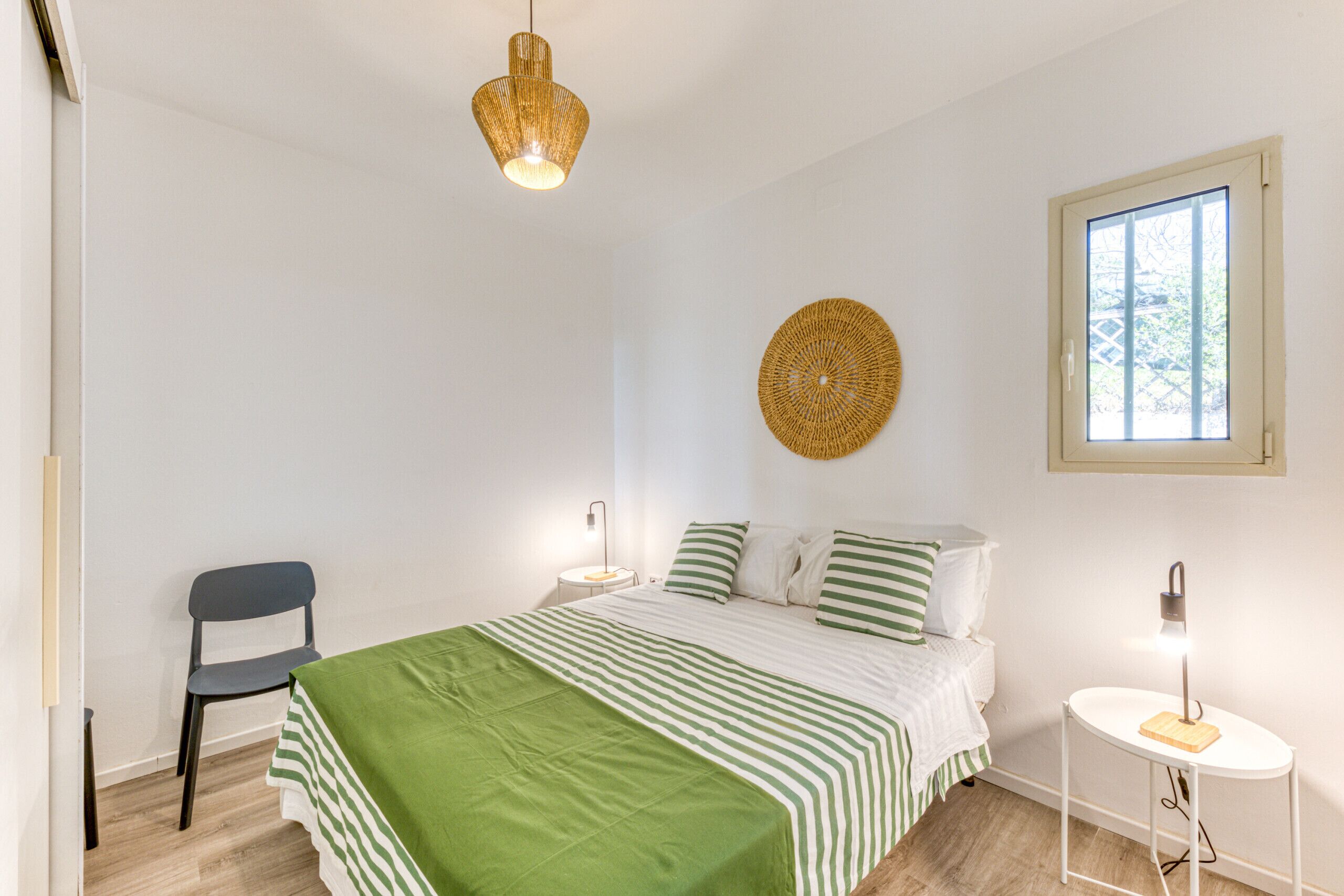 Ein Schlafzimmer mit einem Bett, einem Sessel, einer runden Wanddekoration, einem Fenster und einem Nachttisch mit Lampe.